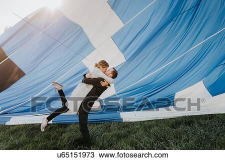 Stock Image - Newly engaged couple kissing, hot air balloon in background. Fotosearch