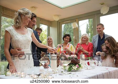 Stock Image - Newlyweds cutting wedding cake at reception. Fotosearch