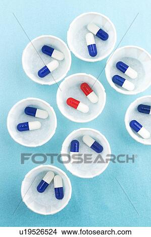 Picture - Paper medicine pots with blue and white capsules and a single dose of red and white capsules.. Fotosearch