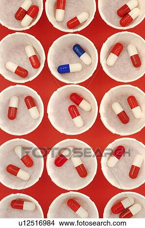 Picture - Paper medicine pots with red and white drug capsules and a single dose of blue and white capsules.. Fotosearch