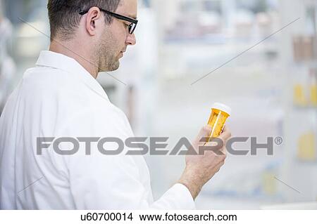 Picture - Pharmacist reading label on pill bottle in pharmacy.. Fotosearch
