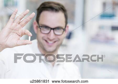 Stock Image - Portrait of smiling pharmacist holding pill.. Fotosearch