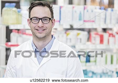 Stock Photo - Portrait of young male pharmacist standing in pharmacy.. Fotosearch