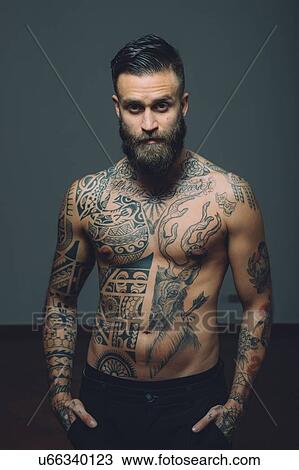 Stock Image - Portrait of young man with beard, bare chest covered in tattoos. Fotosearch