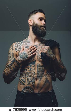 Stock Photography - Portrait of young man with beard, bare chest covered in tattoos. Fotosearch