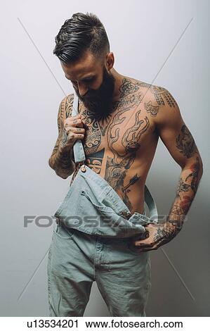 Portrait of young man with wearing dungarees, bare chest covered in tattoos View Large Photo Image Stock Image - Portrait of young man with wearing dungarees, bare chest covered in tattoos. Fotosearch