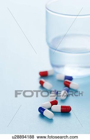 Red and blue drug capsules scattered on a blue background with a glass of water beside them. View Large Photo Image Stock Photo - Red and blue drug capsules scattered on a blue background with a glass of water beside them.. Fotosearch
