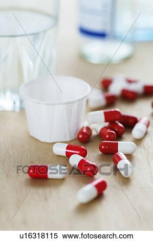 Stock Photography - Red and white drug capsules by a glass of water.. Fotosearch
