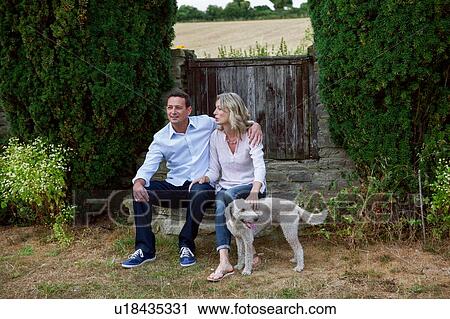 Stock Image - Romantic mature couple with dog sitting in garden. Fotosearch