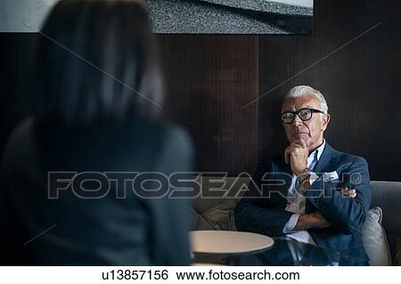 Senior businessman sitting in hotel table meeting with businesswoman, over shoulder view View Large Photo Image Stock Photograph - Senior businessman sitting in hotel table meeting with businesswoman, over shoulder view. Fotosearch