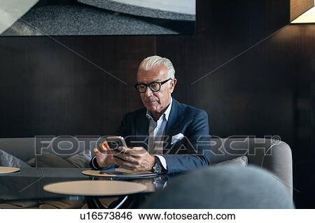 Senior businessman sitting in hotel table using smartphone touchscreen View Large Photo Image Stock Photograph - Senior businessman sitting in hotel table using smartphone touchscreen. Fotosearch