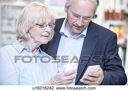 Stock Image - Senior couple checking medicine on mobile phone in pharmacy.. Fotosearch