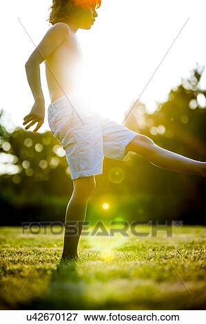 Stock Photo - Shirtless boy stretching his leg in park, backlit.. Fotosearch