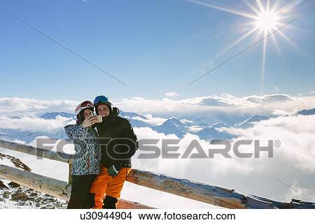 Skiing couple taking smartphone selfie above the clouds, Madonna di Senales, Trentino-Alto Adige, Italy View Large Photo Image Picture - Skiing couple taking smartphone selfie above the clouds, Madonna di Senales, Trentino-Alto Adige, Italy. Fotosearch