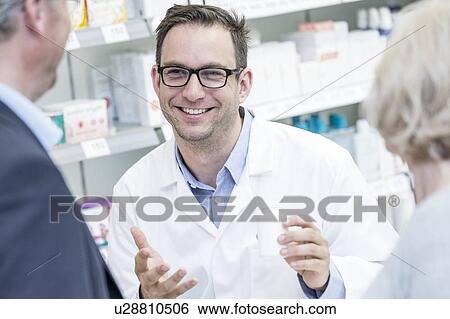 Stock Photograph - Smiling male pharmacist explaining medication to senior customers in pharmacy.. Fotosearch