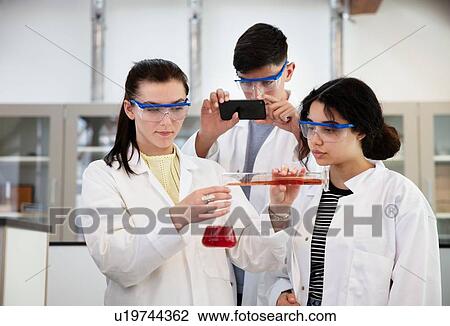 Stock Image - Students pouring sample into flask in laboratory. Fotosearch