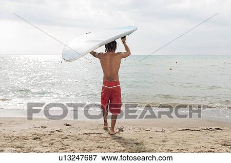 Stock Photo - Surfer with surfboard by seaside. Fotosearch