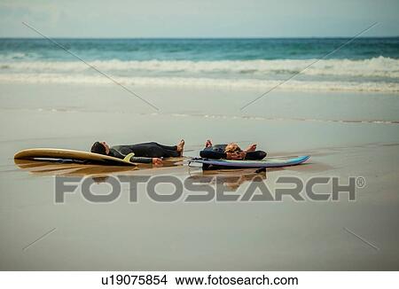 Surfers resting on surfboard at beach, Watergate Bay, Cornwall, UK View Large Photo Image Picture - Surfers resting on surfboard at beach, Watergate Bay, Cornwall, UK. Fotosearch