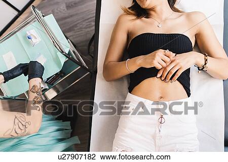 Stock Image - Tattooist attending to customer in parlour. Fotosearch