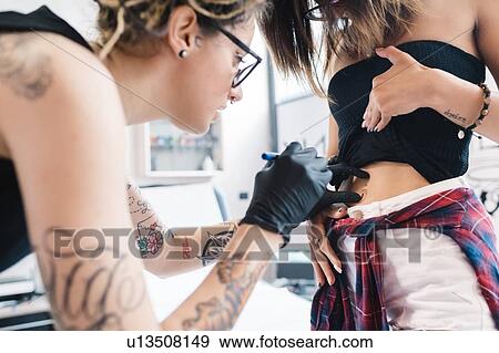 Stock Photo - Tattooist attending to customer in parlour. Fotosearch