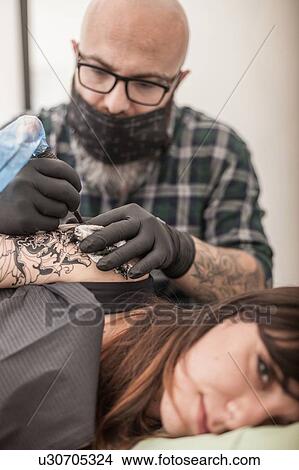 Picture - Tattooist drawing on arm of client. Fotosearch