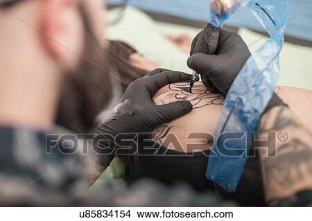 Picture - Tattooist drawing on arm of client. Fotosearch