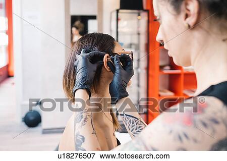 Tattooist piercing ear of customer in parlour View Large Photo Image Stock Photo - Tattooist piercing ear of customer in parlour. Fotosearch
