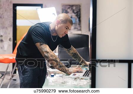 Stock Photo - Tattooist using laptop in parlour. Fotosearch