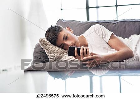 Teenage boy lying on sofa looking at smartphone View Large Photo Image Stock Photography - Teenage boy lying on sofa looking at smartphone. Fotosearch