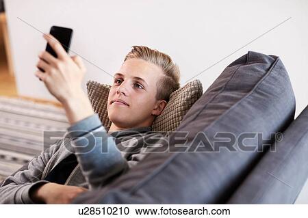 Teenage boy relaxing on sofa looking at smartphone View Large Photo Image Stock Image - Teenage boy relaxing on sofa looking at smartphone. Fotosearch