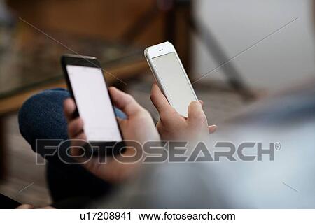 Stock Image - Teenage girl and boy looking at smartphones, close up of hands. Fotosearch