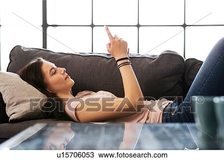 Stock Image - Teenage girl lying on sofa looking at smartphone. Fotosearch