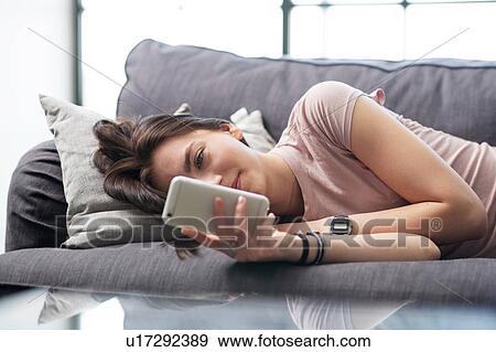 Stock Photo - Teenage girl lying on sofa looking at smartphone. Fotosearch