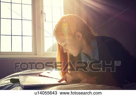 Stock Image - Teenage girl reading in bed. Fotosearch