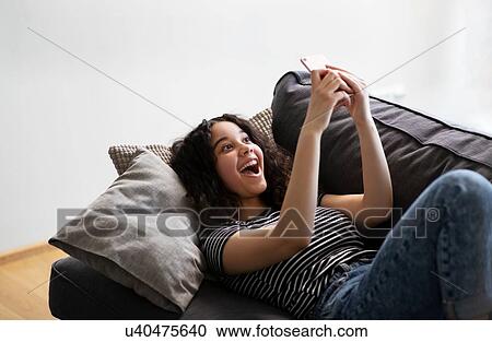 Teenage girl relaxing on sofa laughing at smartphone View Large Photo Image Stock Image - Teenage girl relaxing on sofa laughing at smartphone. Fotosearch