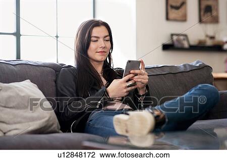 Teenage girl sitting on sofa looking at smartphone View Large Photo Image Stock Image - Teenage girl sitting on sofa looking at smartphone. Fotosearch