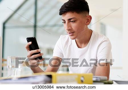 Picture - Teenage schoolboy at classroom desk looking at smartphone. Fotosearch