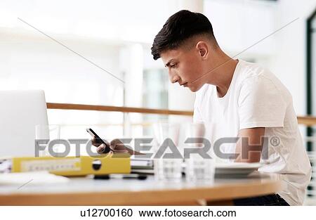 Teenage schoolboy at classroom desk looking at smartphone View Large Photo Image Stock Image - Teenage schoolboy at classroom desk looking at smartphone. Fotosearch