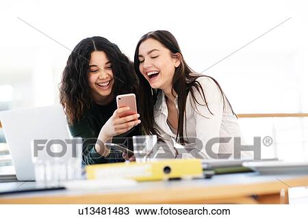 Teenage schoolgirls at classroom desk laughing at smartphone View Large Photo Image Stock Image - Teenage schoolgirls at classroom desk laughing at smartphone. Fotosearch