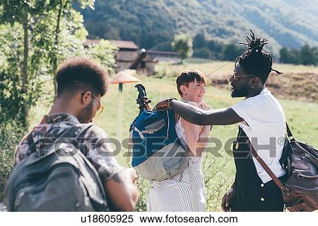 Stock Photography - Three young adult hiking friends preparing rucksacks in field. Fotosearch