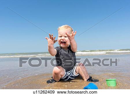 Stock Photo - Toddler horrified with sea water on hands on beach. Fotosearch