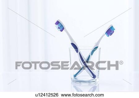 Stock Photograph - Toothbrushes in glass against a plain background.. Fotosearch