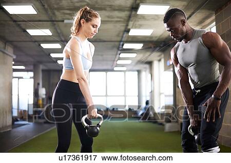 Stock Photo - Trainer and female client exercise with kettlebells in gym. Fotosearch