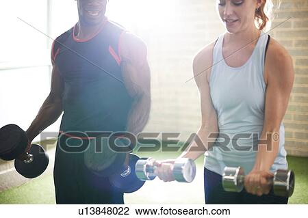 Trainer and female client lifting dumbbells in gym View Large Photo Image Stock Image - Trainer and female client lifting dumbbells in gym. Fotosearch
