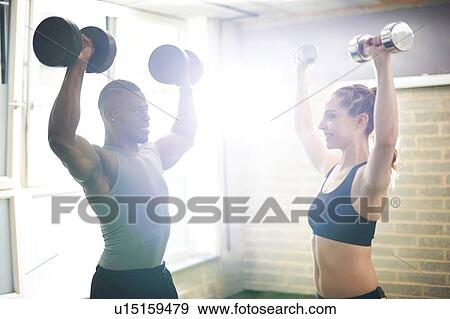 Stock Photo - Trainer and female client lifting dumbbells in gym. Fotosearch