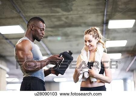 Stock Image - Trainer and female client talking in gym. Fotosearch