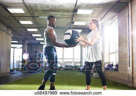 Trainer handing over medicine ball to female client in gym View Large Photo Image Stock Photo - Trainer handing over medicine ball to female client in gym. Fotosearch