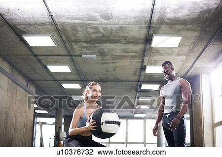 Trainer watching female client lift medicine ball in gym View Large Photo Image Stock Image - Trainer watching female client lift medicine ball in gym. Fotosearch