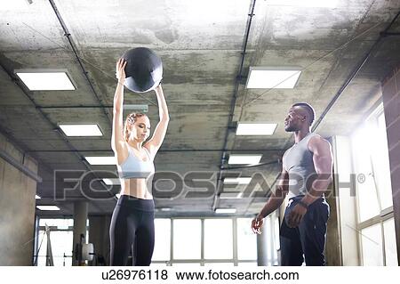 Trainer watching female client lift medicine ball in gym View Large Photo Image Stock Photo - Trainer watching female client lift medicine ball in gym. Fotosearch