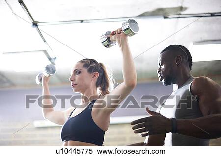 Trainer watching female client lifting dumbbells in gym View Large Photo Image Stock Photography - Trainer watching female client lifting dumbbells in gym. Fotosearch